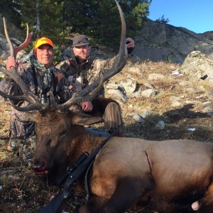 A hunter and his guide posing with his bull elk on a rocky hillside