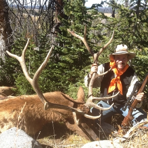 Hunter with an orange scarf holding his rifle and the horns of his bull elk